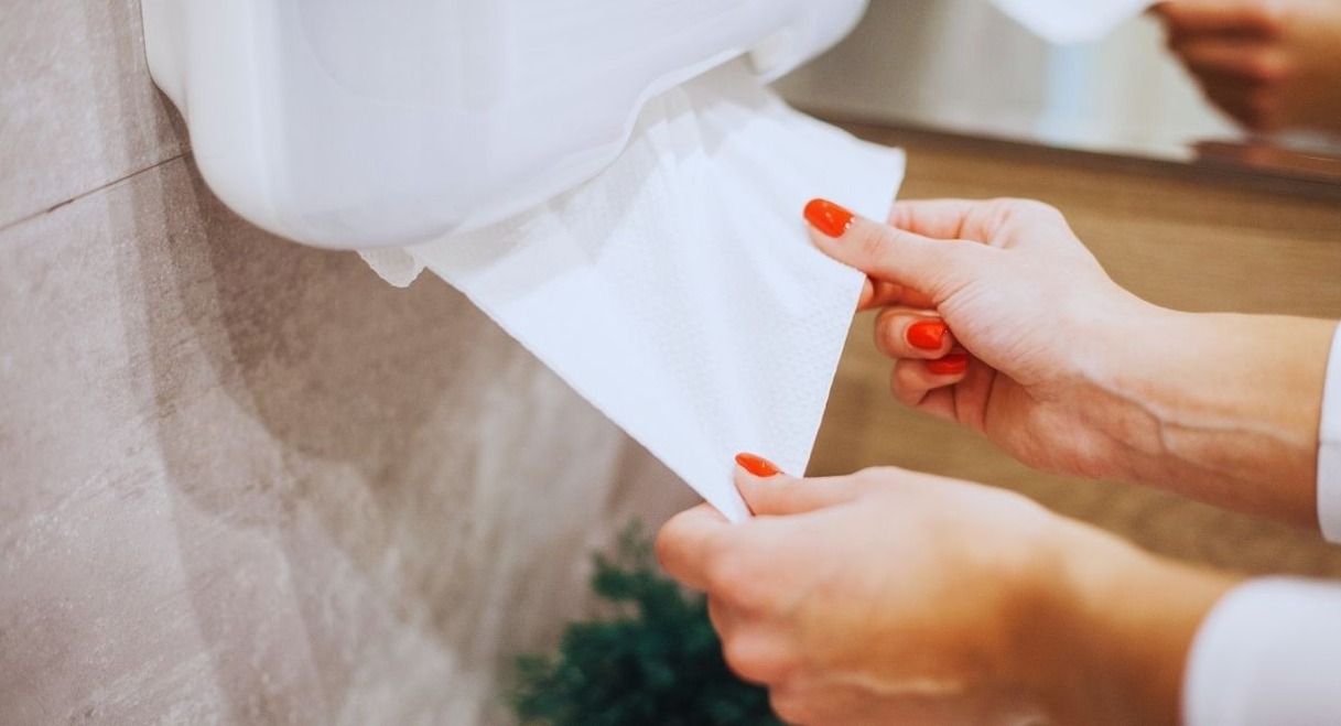 Mains de femme retirant une feuille d'essuie-mains en papier d'un distributeur mural dans des sanitaires